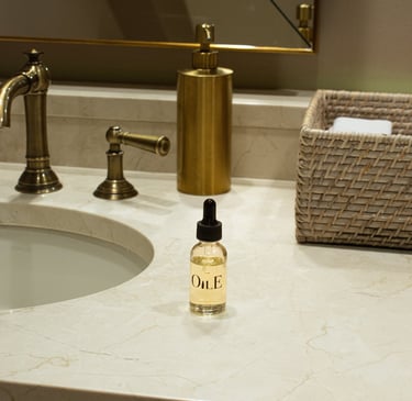 Glass bottle of luxury facial oil with dropper on a marble bathroom vanity next to gold fixtures.