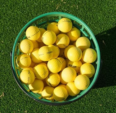 A green plastic basket filled with yellow golf balls on a synthetic grass practice green.