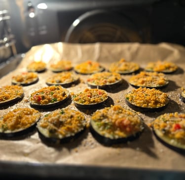 Slices of roasted eggplant with breadcrumb topping baking on a parchment-lined tray in an oven.