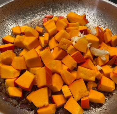 Diced pieces of fresh Hokkaido pumpkin being sautéed in a stainless steel pan with onions.