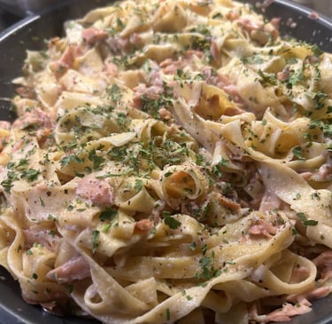 Creamy salmon tagliatelle pasta seasoned with fresh herbs and black pepper in a pan.
