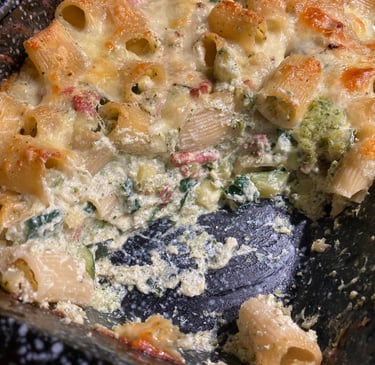 Baked rigatoni pasta with melted cheese, broccoli, and creamy white sauce in a baking dish.