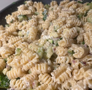 Creamy radiatori pasta salad with diced cucumbers and fresh herbs in a large bowl.