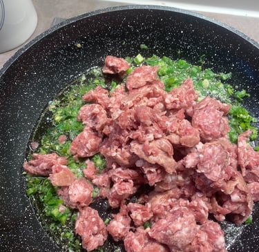 Raw ground sausage browning in a skillet with sautéed green onions and oil.