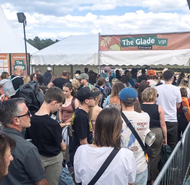 A crowd of people waits in a long queue at the Glade VIP entrance of an outdoor music festival.