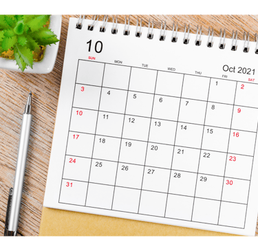 October 2021 monthly desk calendar on a wooden surface with a pen and small green plant.