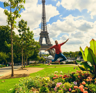 A happy man jumps in the air in front of the Eiffel Tower in Paris, France, on a sunny day.