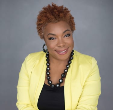 A woman weasring a yellow blazer with a black shirt underneath.  She's wearing a black necklace an d