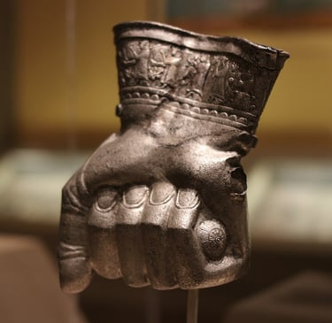 Ancient Hittite silver fist-shaped vessel with detailed relief carvings on the wrist displayed in a museum.