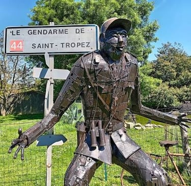 A metal sculpture of Le Gendarme de Saint-Tropez standing next to a French road sign.