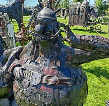 Whimsical scrap metal sculpture of cartoon character Obelix in an outdoor art garden.