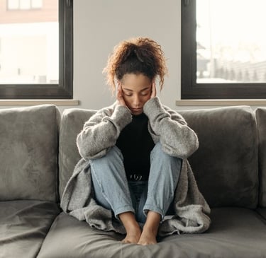 A stressed woman sitting on a couch holding her head, illustrating mental health and anxiety relief.