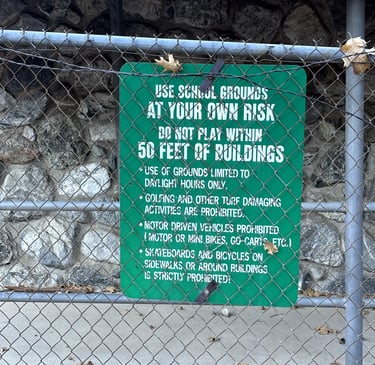 Green “Use School Grounds at Your Own Risk” sign on fence at Fallsvale Schoolhouse.