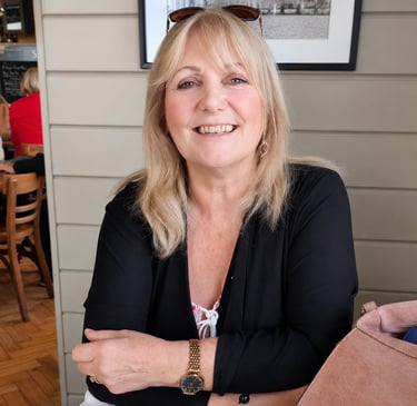 Maureen Chaloner wearing a black cardigan and gold watch sitting in a cafe.