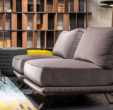 Modern grey velvet lounge chair in a luxury living room with a wooden bookshelf and colorful area rug.
