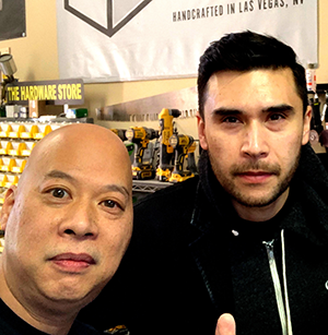 Ray Lum and Dan White posing for a selfie in KMD shop with power tools and saws in the background.
