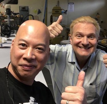 Ray and Jeff Hobson giving thumbs up in a woodworking workshop with power tools in the background.