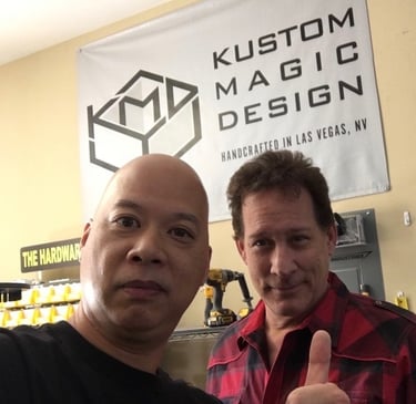 Ray and Mark Kalin standing in front of a Kustom Magic Design banner in a Las Vegas workshop.