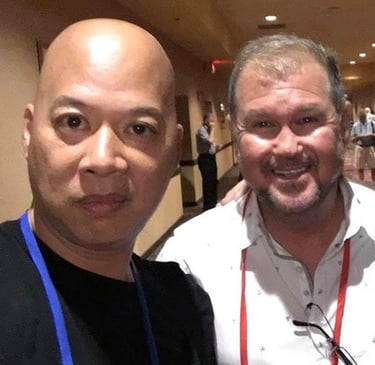 Ray Lum and Daniel Summer taking a selfie together at a conference event in a hotel hallway.
