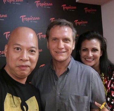 Three people smiling at a Tropicana Las Vegas event with a branded logo backdrop.