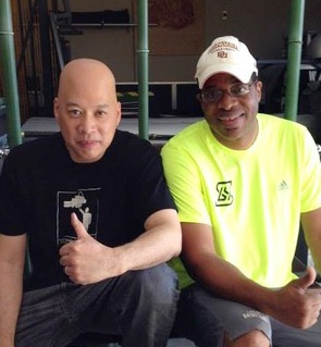 Two men posing for a photo at the gym, giving a thumbs up while wearing athletic gear.