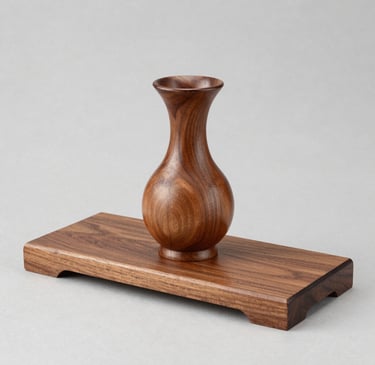 A sleek, modern vase with a smooth matte finish sitting on a wooden shelf against a soft neutral wall.