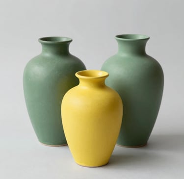 A sleek, modern vase with a smooth matte finish sitting on a wooden shelf against a soft neutral wall.
