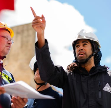 Professional construction site supervisor in a hard hat pointing toward project plans during a team meeting.