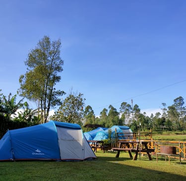 Tenda camping biru di area perkemahan alam terbuka Pangalengan dengan pemandangan pepohonan hijau dan langit biru cerah