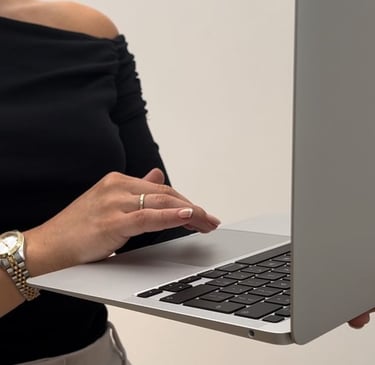 Woman in a black off-shoulder top working on a laptop, holding it with one hand while typing.