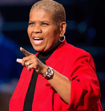 a woman in a red jacket and black top speaking to a crowd