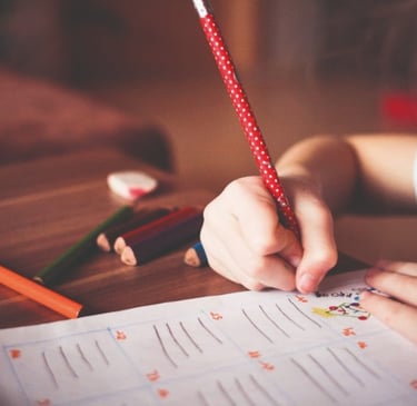 Main d'un enfant tenant fermement un crayon à pois rouges, s'appliquant à un exercice d'écriture, une technique encouragée pa