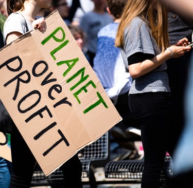 Crowd at climate change rally with focus on sign 'PLANET OVER PROFIT', highlighting green initiative