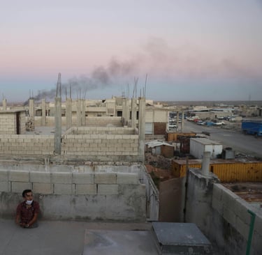 A child sits alone on a rooftop in a conflict zone, symbolizing the personal impact of forced migration and the resilience of