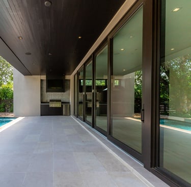 the outside patio of a luxury home with an outdoor grill, pool and deck with sliding glass doors