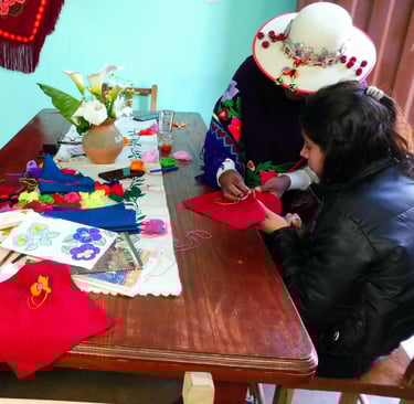 turistas y artesanas bordando juntas sentadas alrededor de una mesa
