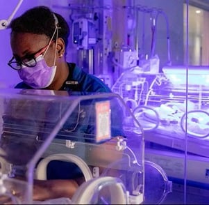 African nurse wearing mask tending baby in an ICU (Photo courtesy of the APFP)
