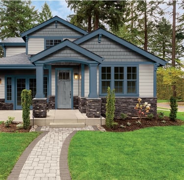 A beautifully painted two-story home with blue and gray exterior tones, stone accents, and a welcom