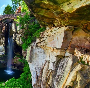 Lookout Mtn, GA - A view looking up at a stone footbridge & waterfall at the clifftop of Rock City