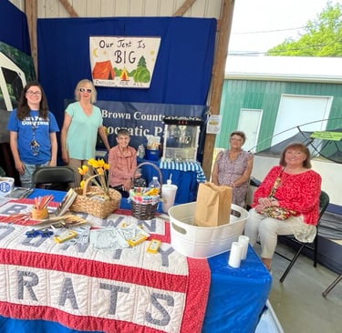 Five women sit or stand behind the Democrats booth at the fair