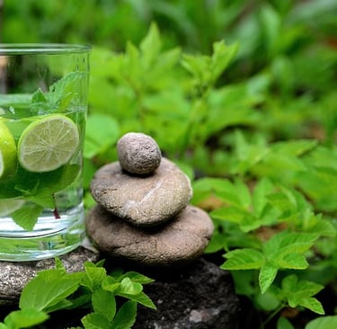 zen-artig angeordnete Steine mit einem Glas infused Wasser mit Limetten inmitten von Minze eingehüllt