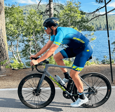 A man on a bike wearing a cycling kit in the outdoors by a lake