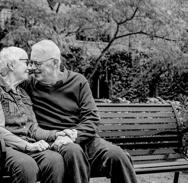 couple de personnes âgées se tenant la main, assis sur un banc