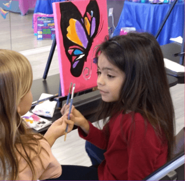 two little girls painting a butterfly on a canvas