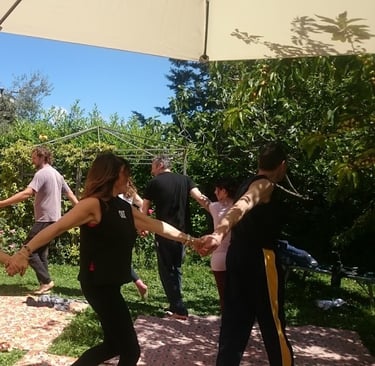 a group of people holding hands and dancing in a garden, classe di bioenergetica