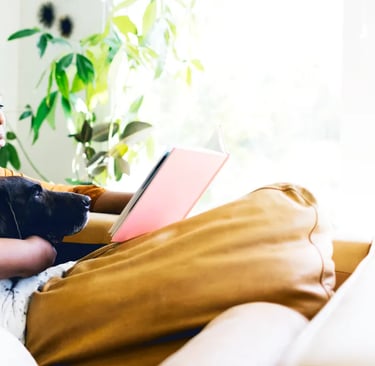 Una mujer afro sentada en un sofá con un perro y leyendo
