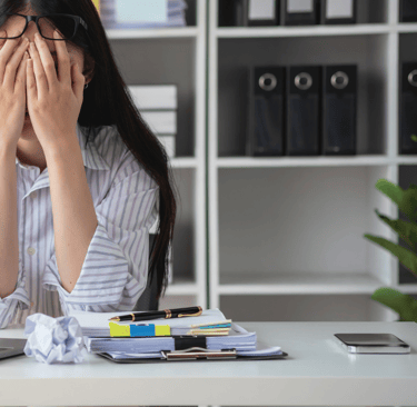 a woman sitting at a desk with her hands covering her face