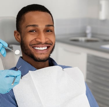 A smiling man as a dentist holds instruments nearby.