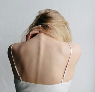 Woman with bare back and blonde hair holding her neck, symbolizing tension, pain, or vulnerability.