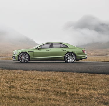 a green bentley driving down a road with a mountain in the background